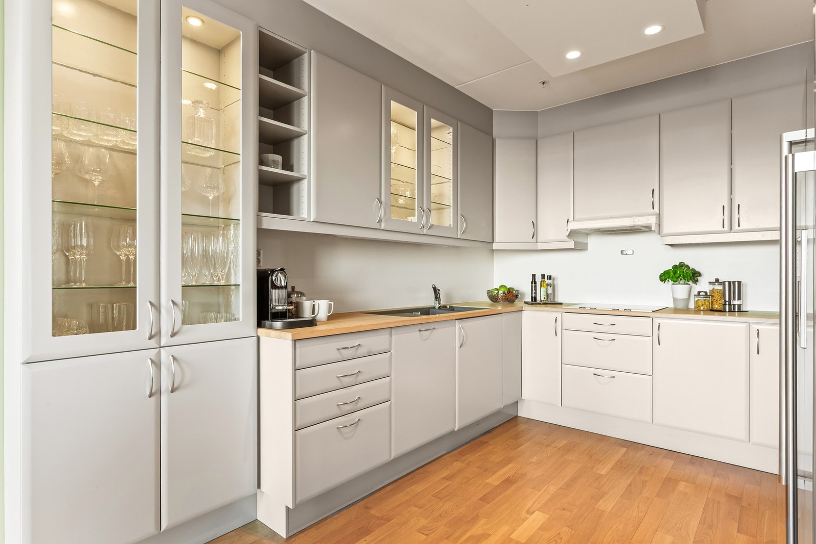 Sigdal kjøkkeninnredning med glatte fronter og vitrinefronter, benkeplate i heltre med nedfelt kum i kompositt og integrerte hvitevarer. Komfyrvakt og aquastopp med sensor er installert. Galleribilde