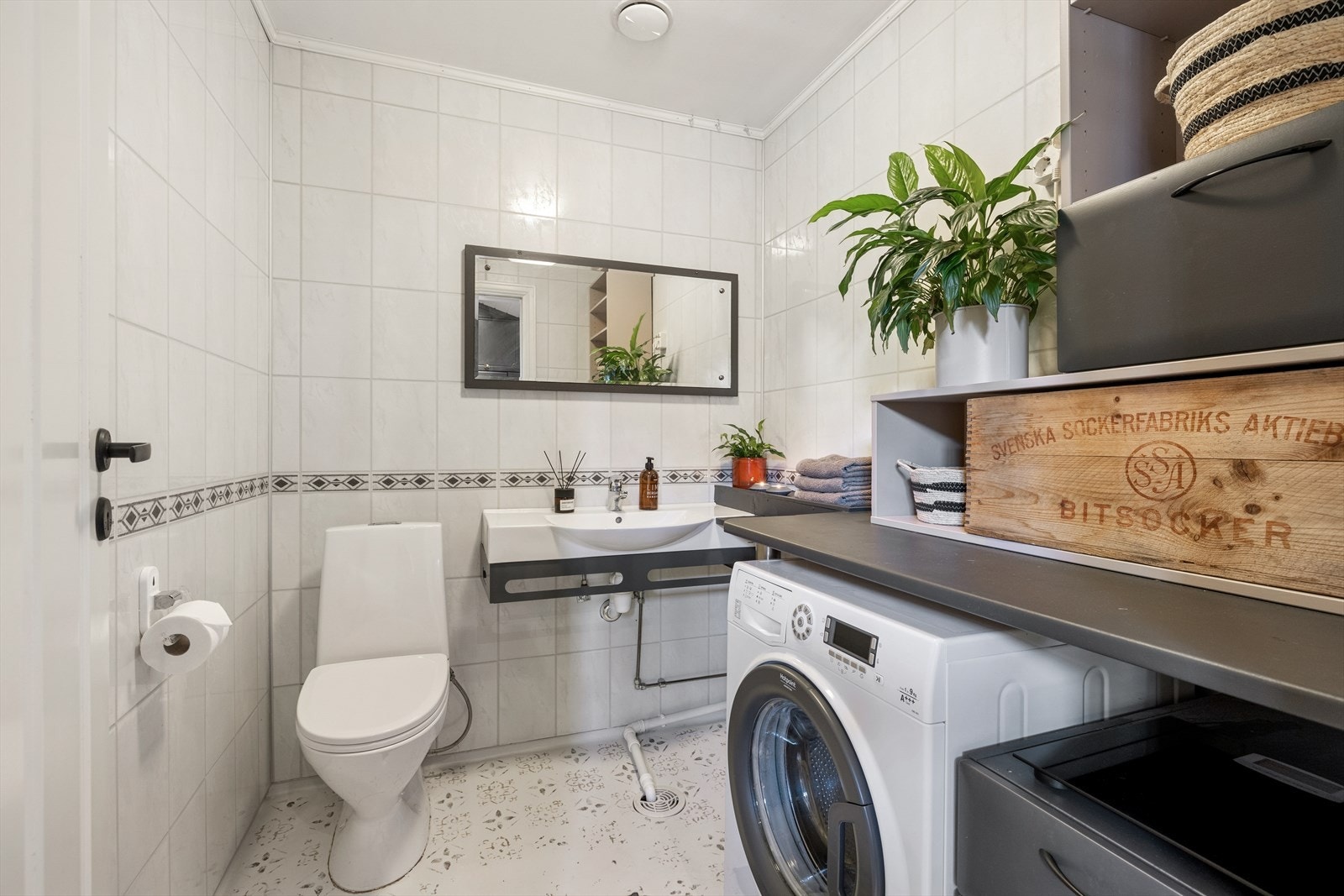 Bad/vaskerom med belegg på gulv og våtromsplater på vegg. Rommet er utstyrt med toalett, servant, innredning, benkeplate og opplegg for vaskemaskin. Galleribilde