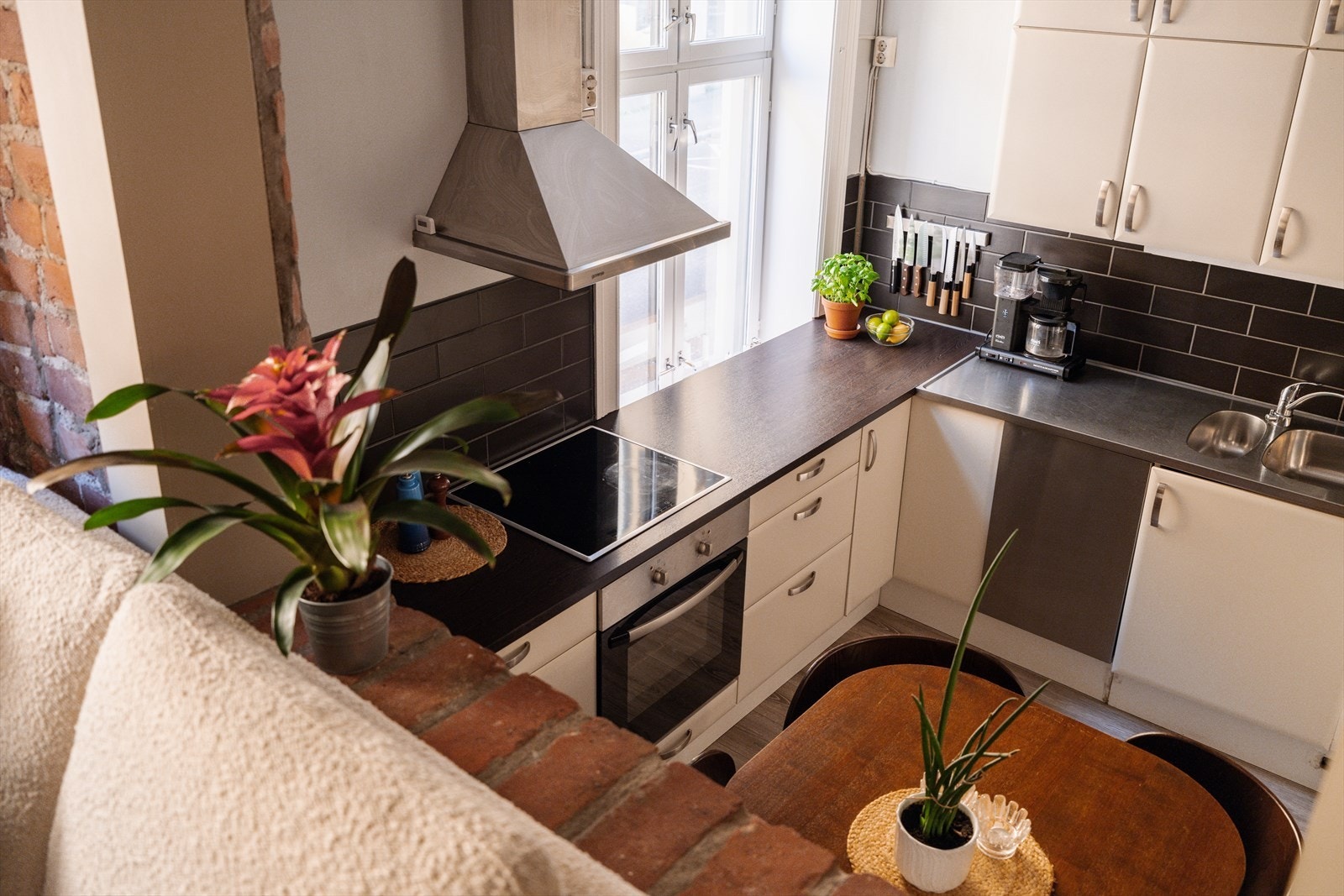 Kjøkkenet har en funksjonell og tidløs utforming med glatte, fabrikklakkerte fronter og laminert benkeplate med nedfelt, heldekkende kum i rustfritt stål. Over benkeplaten er det lagt fliser, og belysningen ivaretas av lystoffrør montert under overskapene Galleribilde