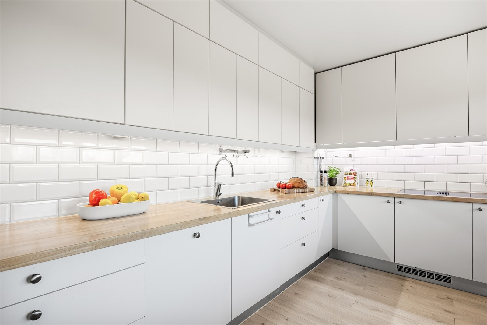 HTH og IKEA innredning med forskjellige årstall som har hvite, glatte fronter og heltre benkeplate med nedfelt kum i rustfritt stål. Galleribilde