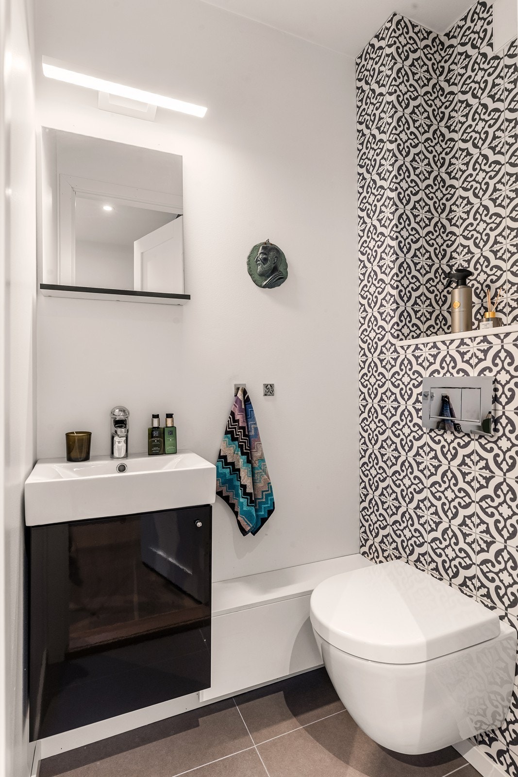 Toalettrommet har fliser på gulvet og dels flislagte vegger, med veggmontert klosett og enkel servant. Galleribilde