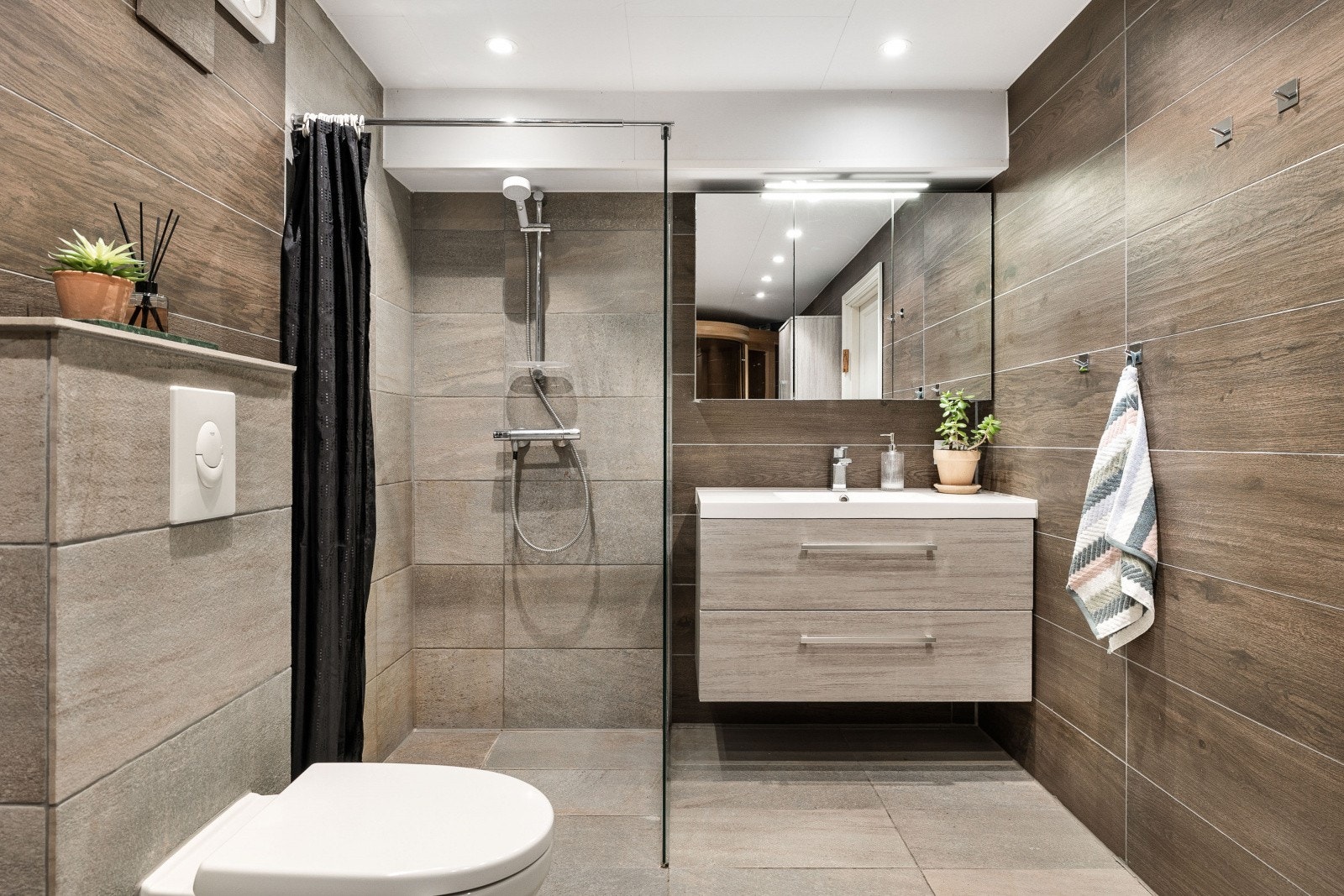 Badet er utstyrt med vegghengt wc, servant med skuffer, speilskap, dusj med glassvegger og badstue Galleribilde