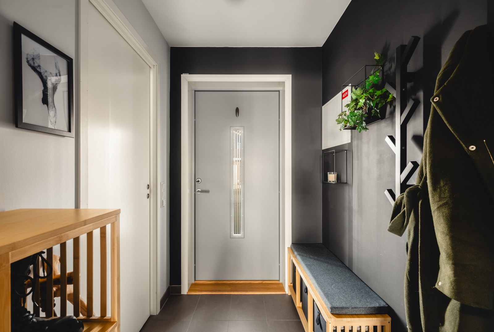 Entreen har mørke vegger, grå inngangsdør og praktisk innredning for oppbevaring. Galleribilde