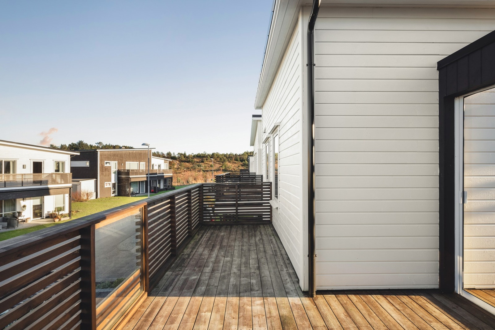 En moderne terrasse med tredekke og rekkverk, omgitt av flere boliger i et nabolag. Galleribilde