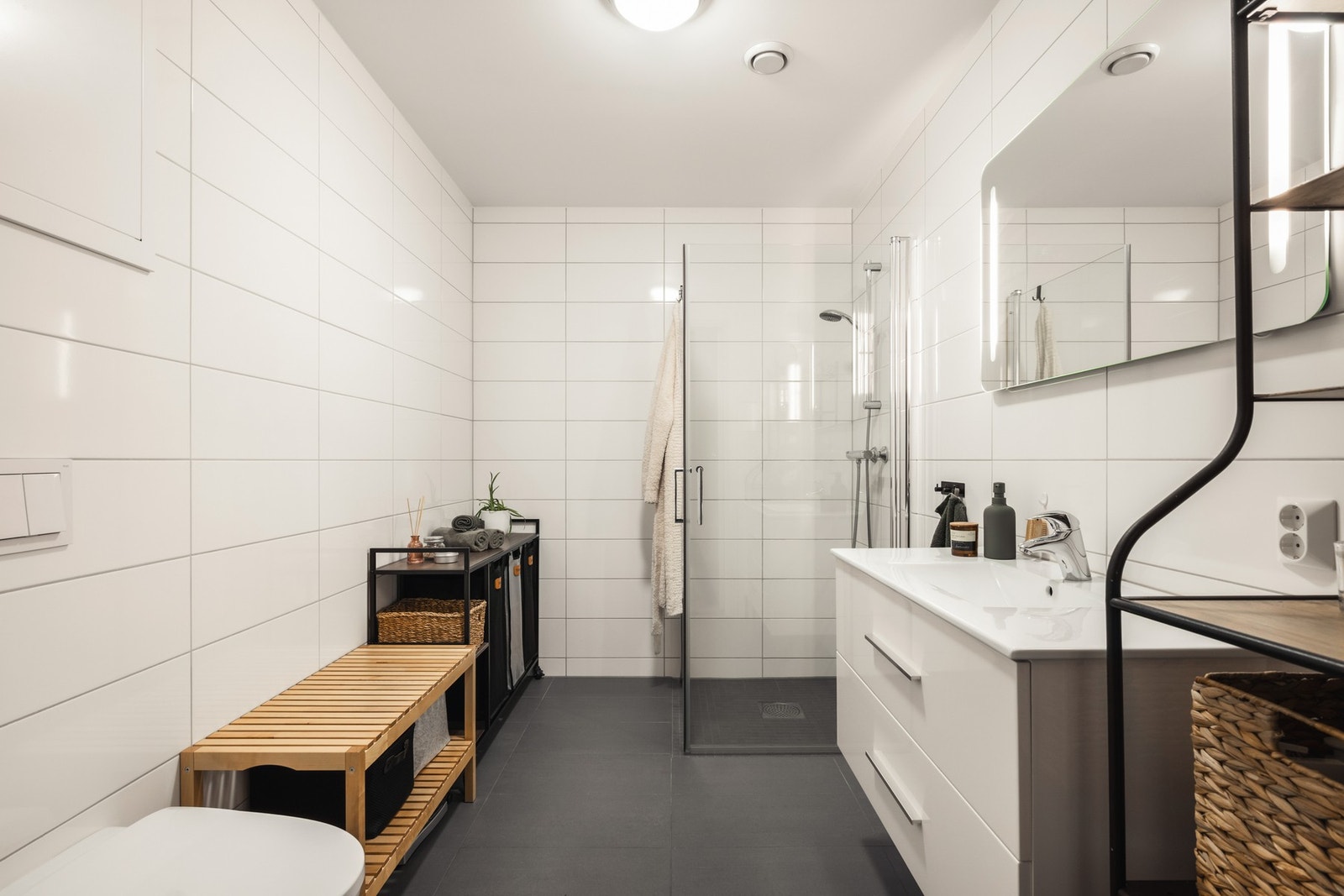 Badet har moderne innredning, dusjkabinett med glassdør, hvite fliser på veggene og mørke fliser på gulvet. Galleribilde