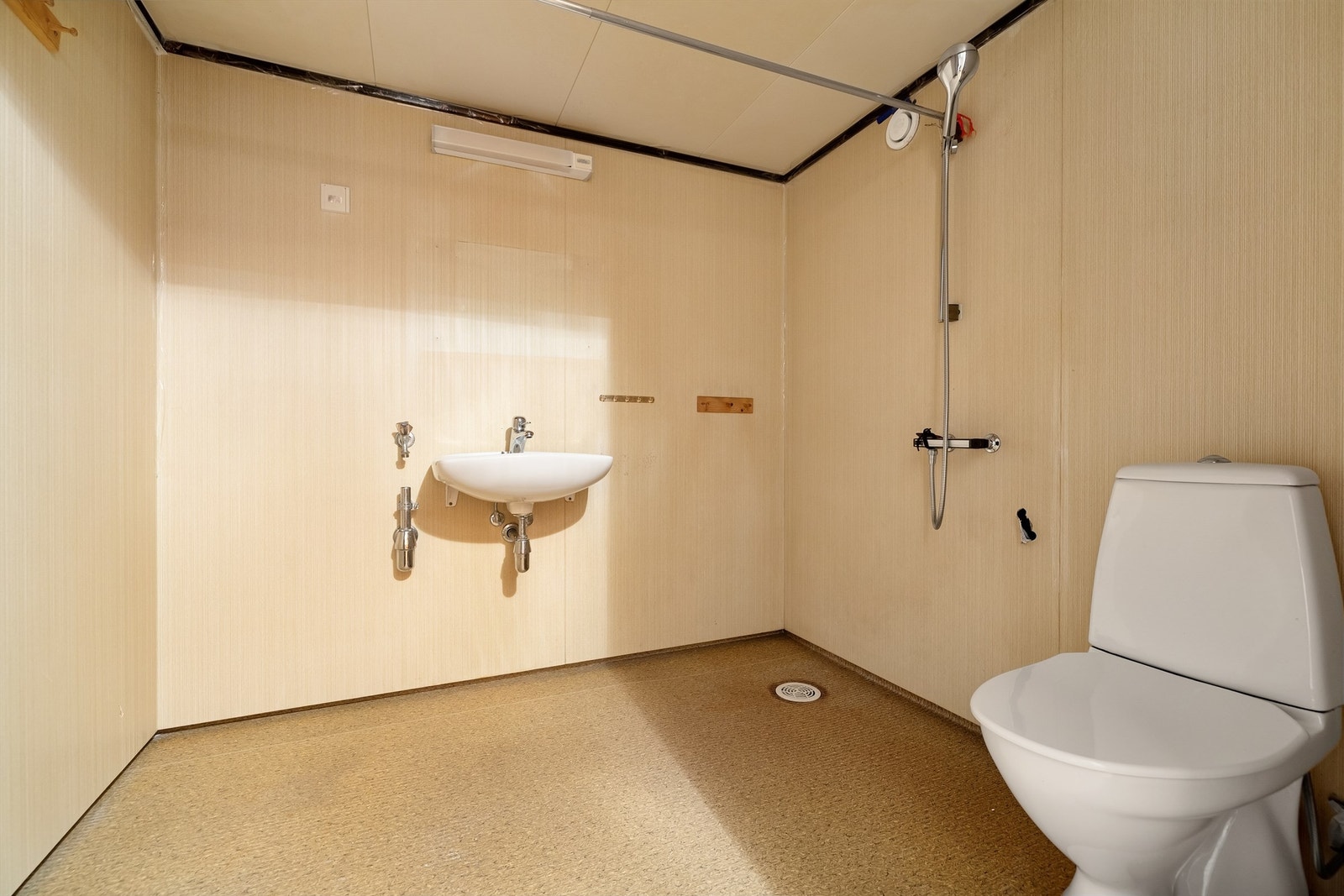 Bad med fin størrelse. Gulvflate belagt med gulvbelegg, vegger med baderomsplater, vegghengt servant med ett-greps blandebatteri, belysning med stikkontakt på vegg over servant, dusj på gulv samt gulvstående toalett. Badet har opplegg for vaskemaskin. Galleribilde