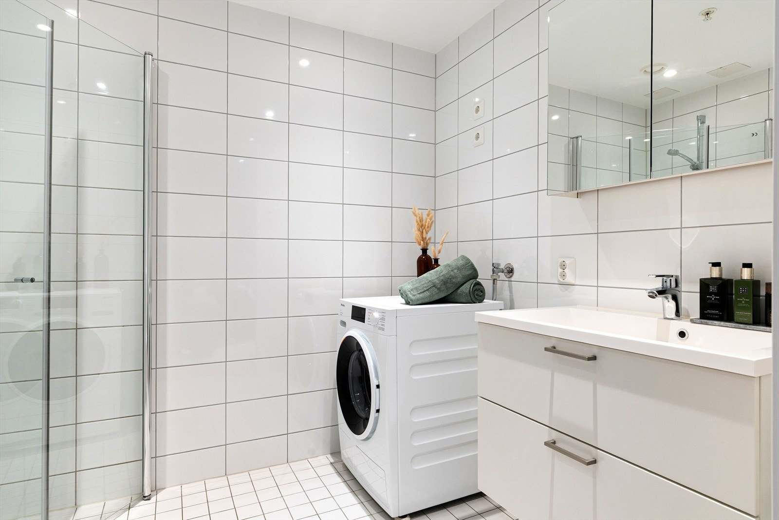 Badet er innredet med servantskap med nedfelt servant, veggskap med speildører samt vegghengt klosett. Dusjsonen har innfelte dusjdører i herdet glass, og det er i tillegg opplegg for vaskemaskin. Galleribilde