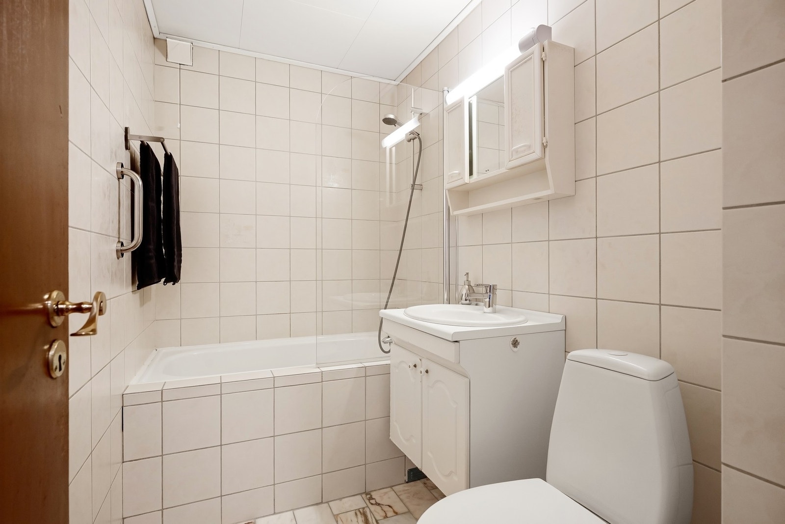 Badet er innredet med servantseksjon med skap, innfliset badekar og gulvmontert toalett. Galleribilde