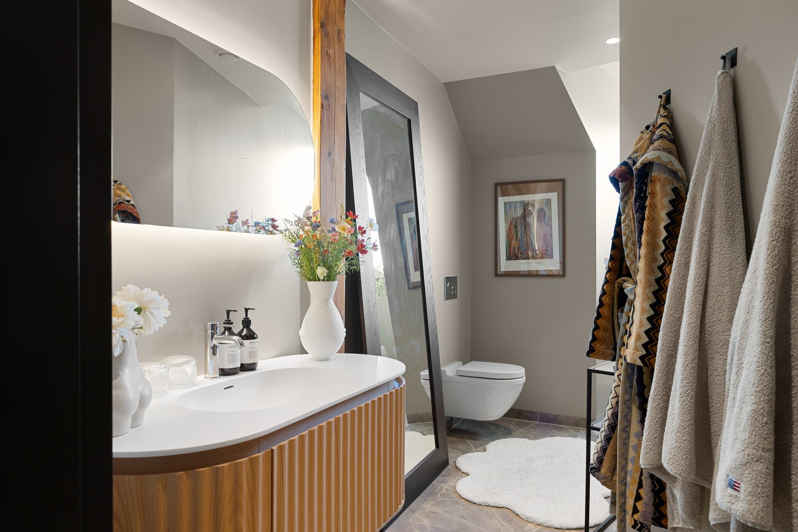 Masterbad er innredet med matchende ovalt speil med indirekte belysning, veggmontert toalett og dusjsone. Galleribilde