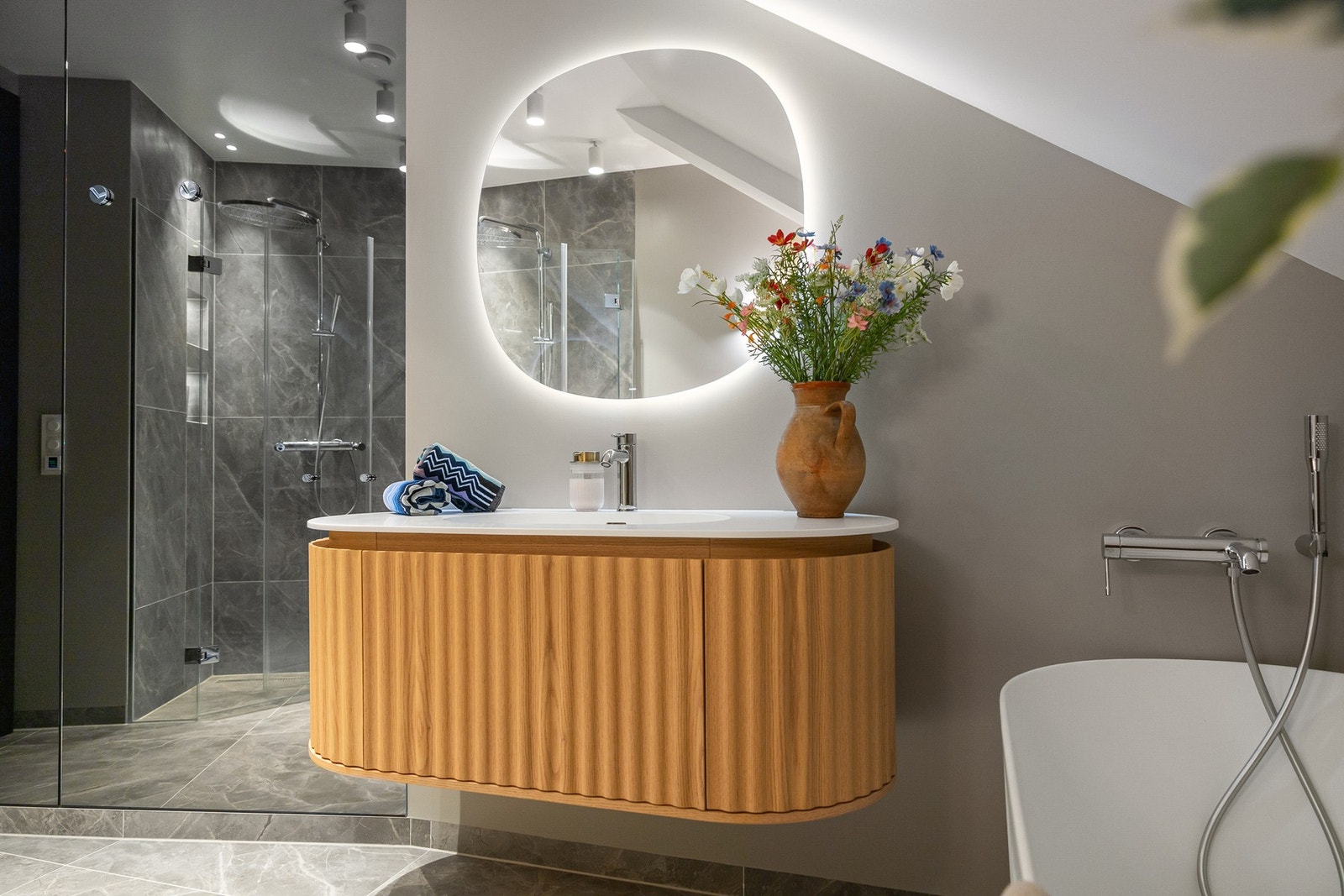 Gjestebad er innredet med et stilig, frittstående designbadekar med hvite rillefronter. Oval servant i corian på eikemøbel med ovale rillefronter matcher badekaret. Galleribilde