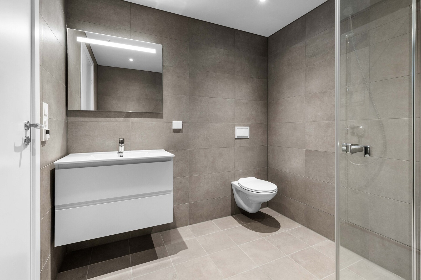 Veggene er kledd med grå fliser i 30x60 cm format, mens gulvet har matchende fliser i 30x30 cm. Galleribilde