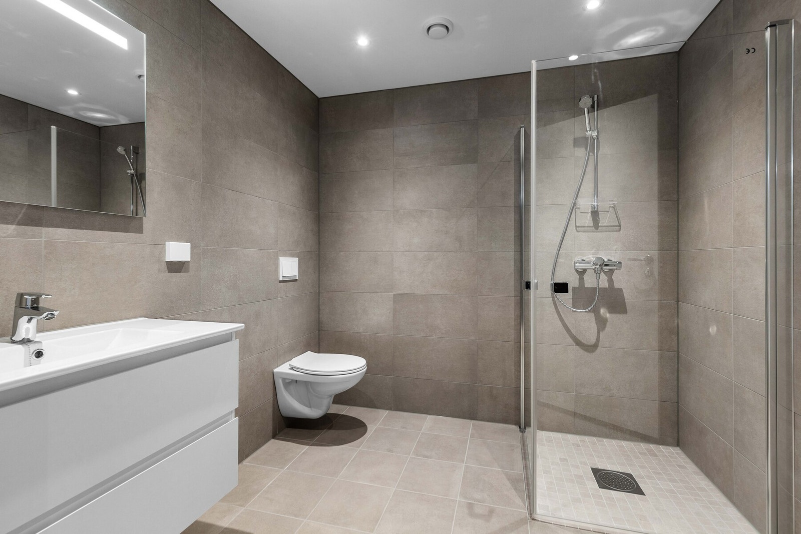 Innredningen består av et moderne baderomsmøbel med to skuffer og heldekkende servant, samt et firkantet speil med integrert belysning. Galleribilde