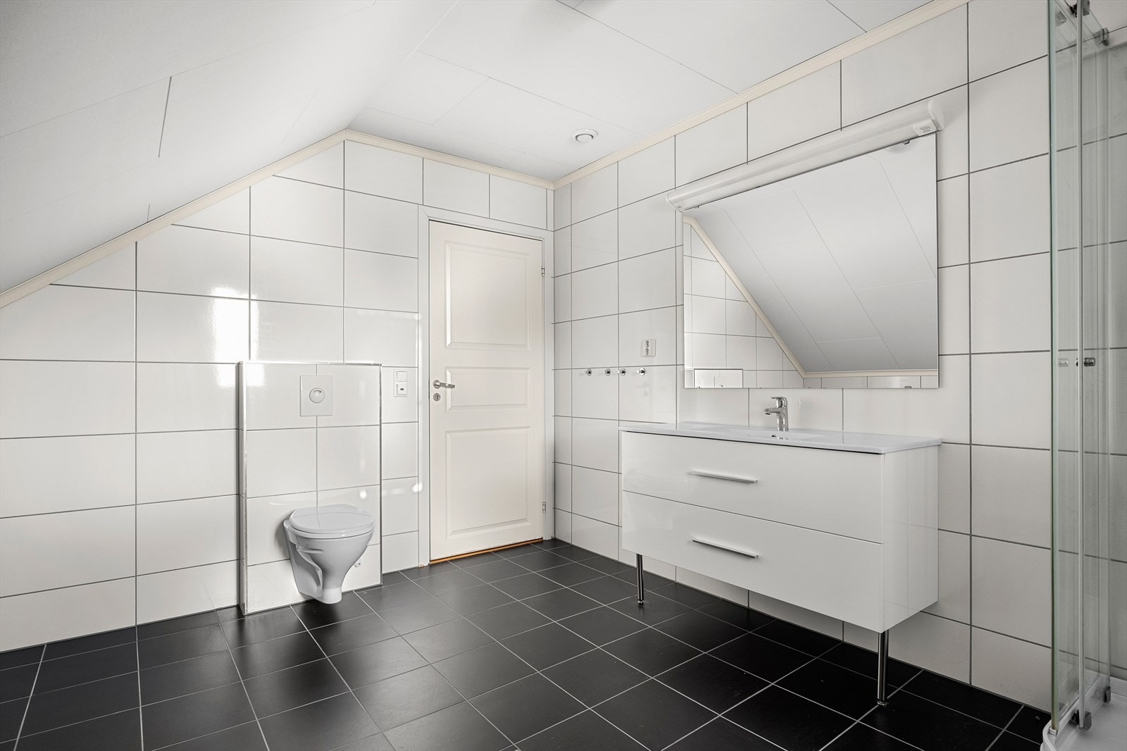 Badet er innredet med dusjkabinett, veggmontert toalett, innredning med servant og opplegg for vaskemaskin (Kran og avløp). Galleribilde