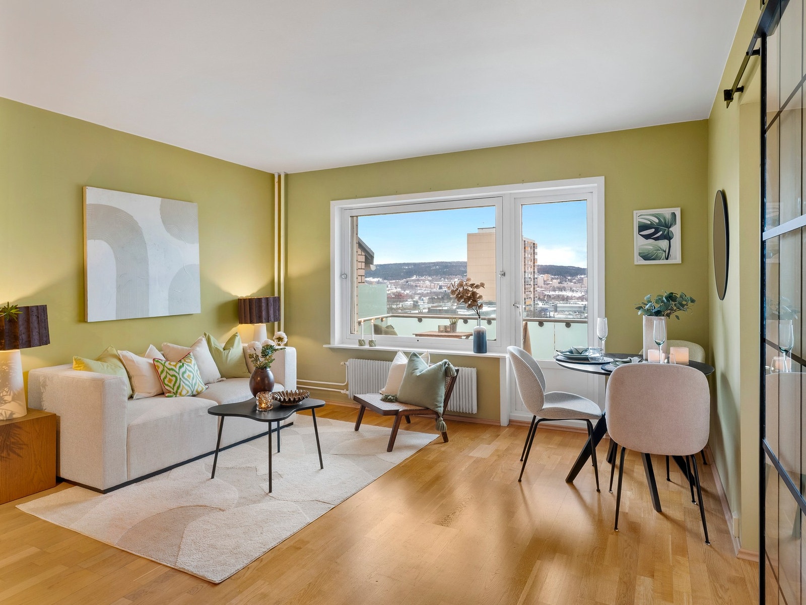 Romslig og lys stue med parkettgulv og store vindusflater, samt utgang til leilighetens balkong Galleribilde