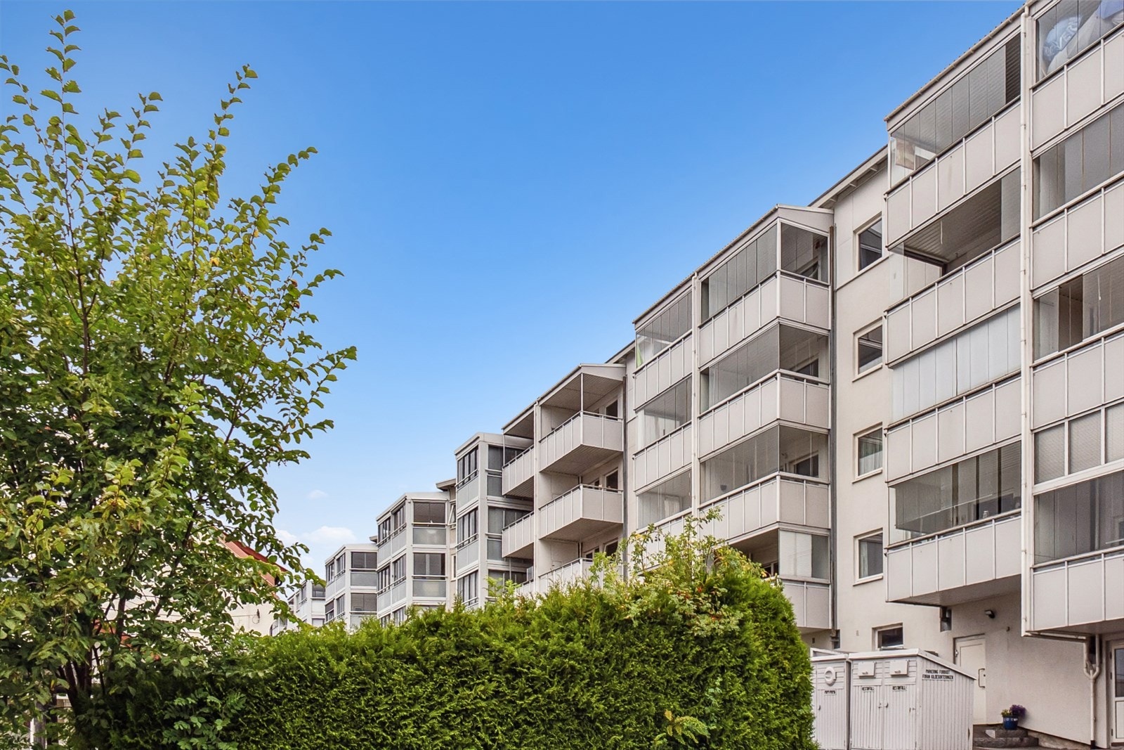 Pent opparbeidet felleshage foran bygget med plen, sittegrupper og beplantning. Galleribilde