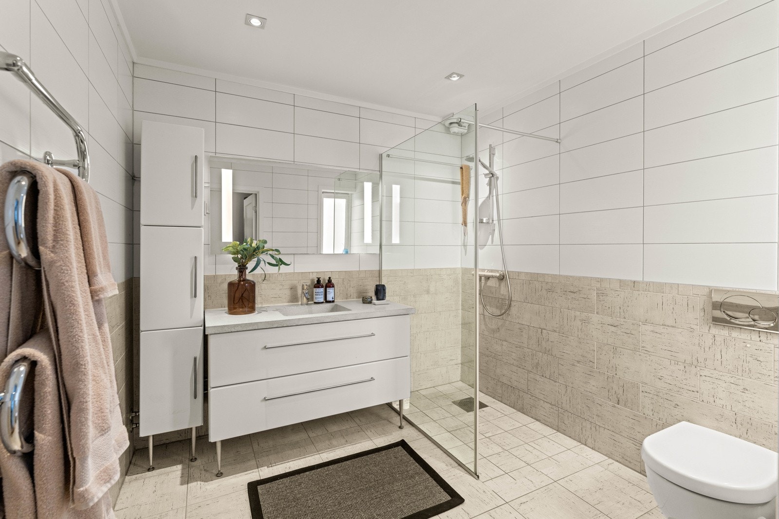 Flislagt bad med varmekabler, dusj med glassvegg og servant med underskuffer Galleribilde