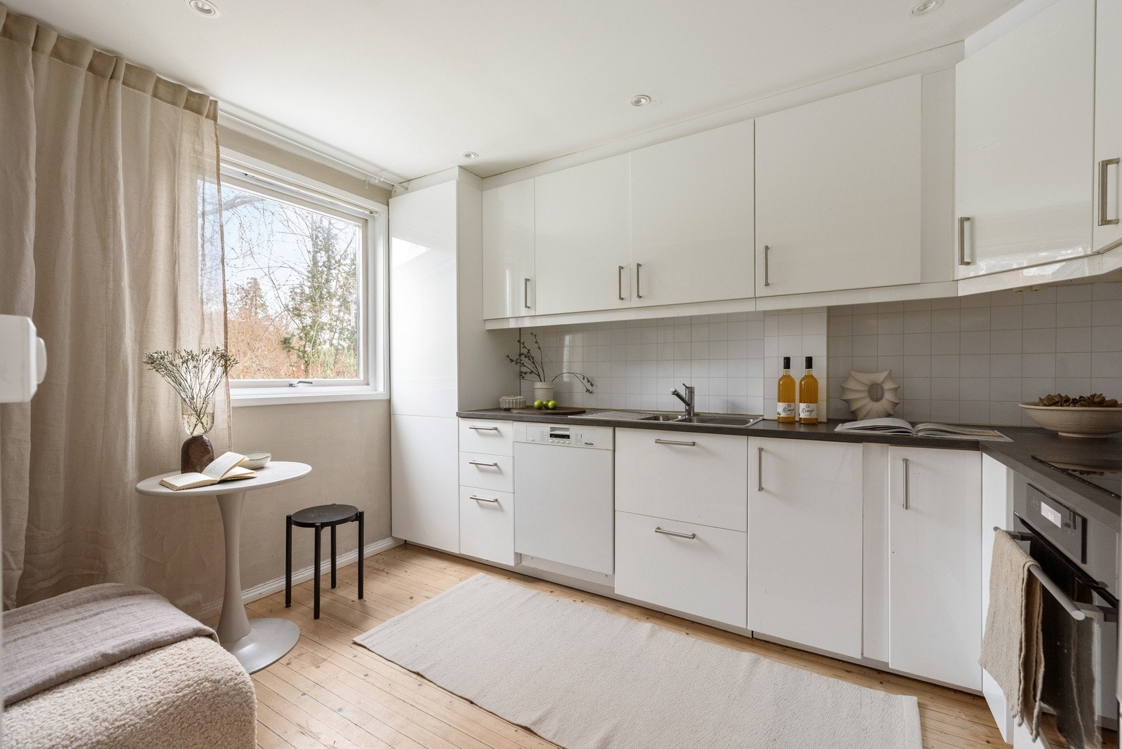 Pent kjøkken fra 2017 med hvite høyglans fronter, laminat benkeplater og intergrerte hvitevarer. Galleribilde