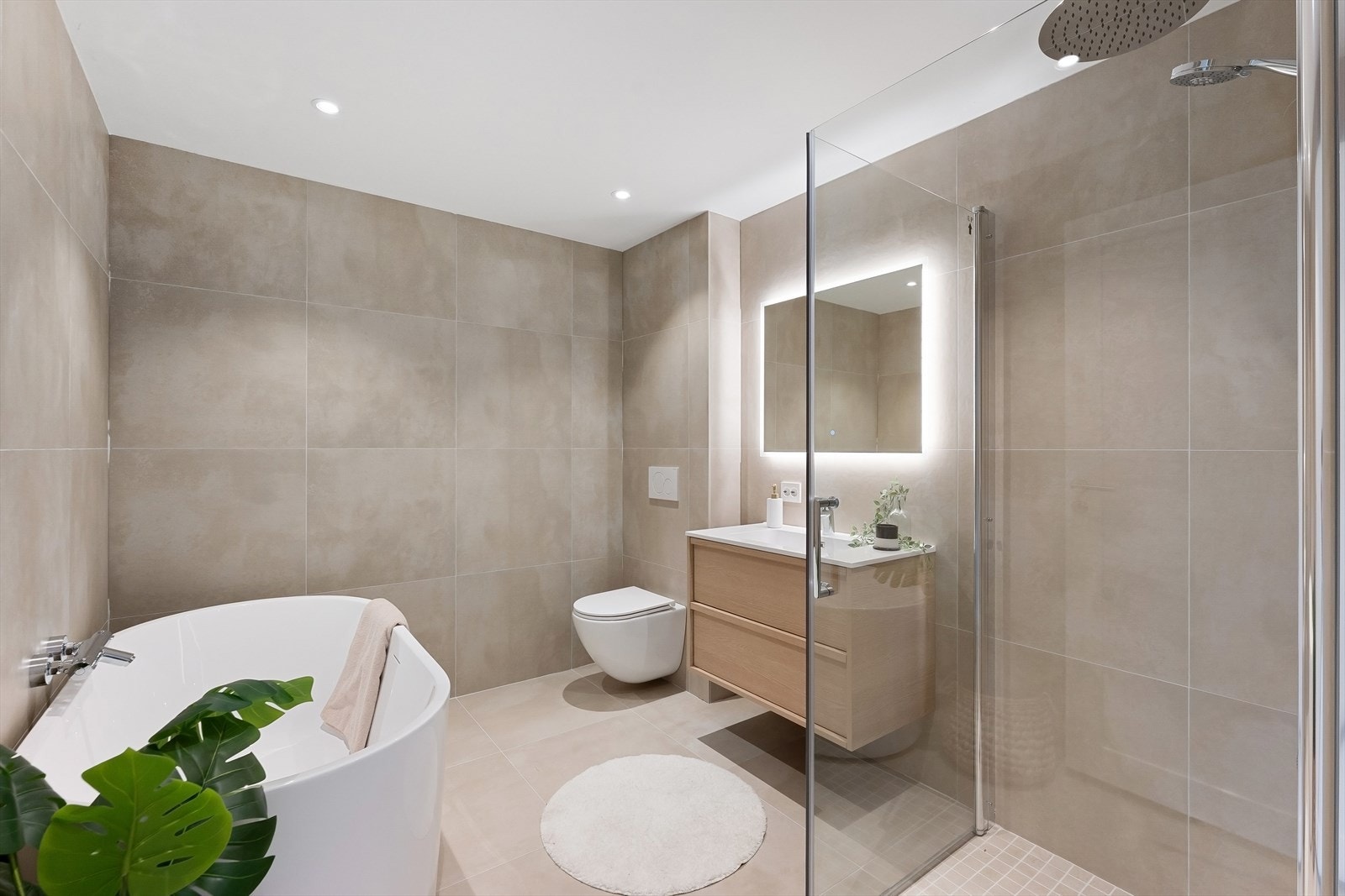 Bad fra 2025 med frittstående badekar, dusjhjørne med dører i herdet glass, speil med LED lys over servant og vegghengt toalett. Galleribilde