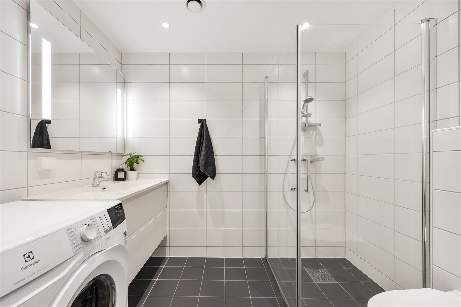 Badet er innredet med servant i baderomsinnredning, speil med integrerte belysning, dusjhjørne og vegghengt toalett. Det er opplegg for vaskemaskin. Galleribilde