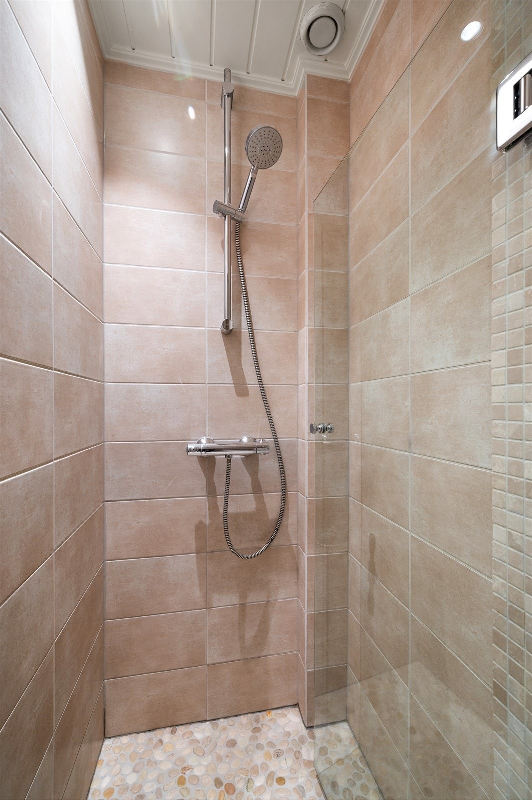 Dusjhjørnet har en elegant glassvegg og dekorative rullesteinsfliser på gulvet. Galleribilde