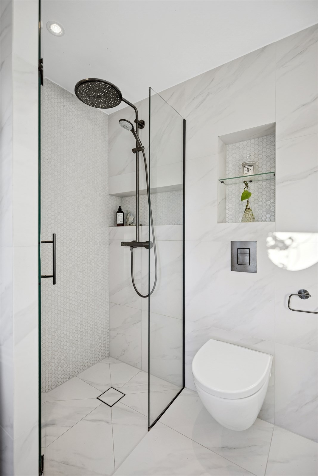 Dusjnisje med glassdør og ettgreps dusjarmatur, samt vegghengt toalett med innebygget sisterne. Galleribilde