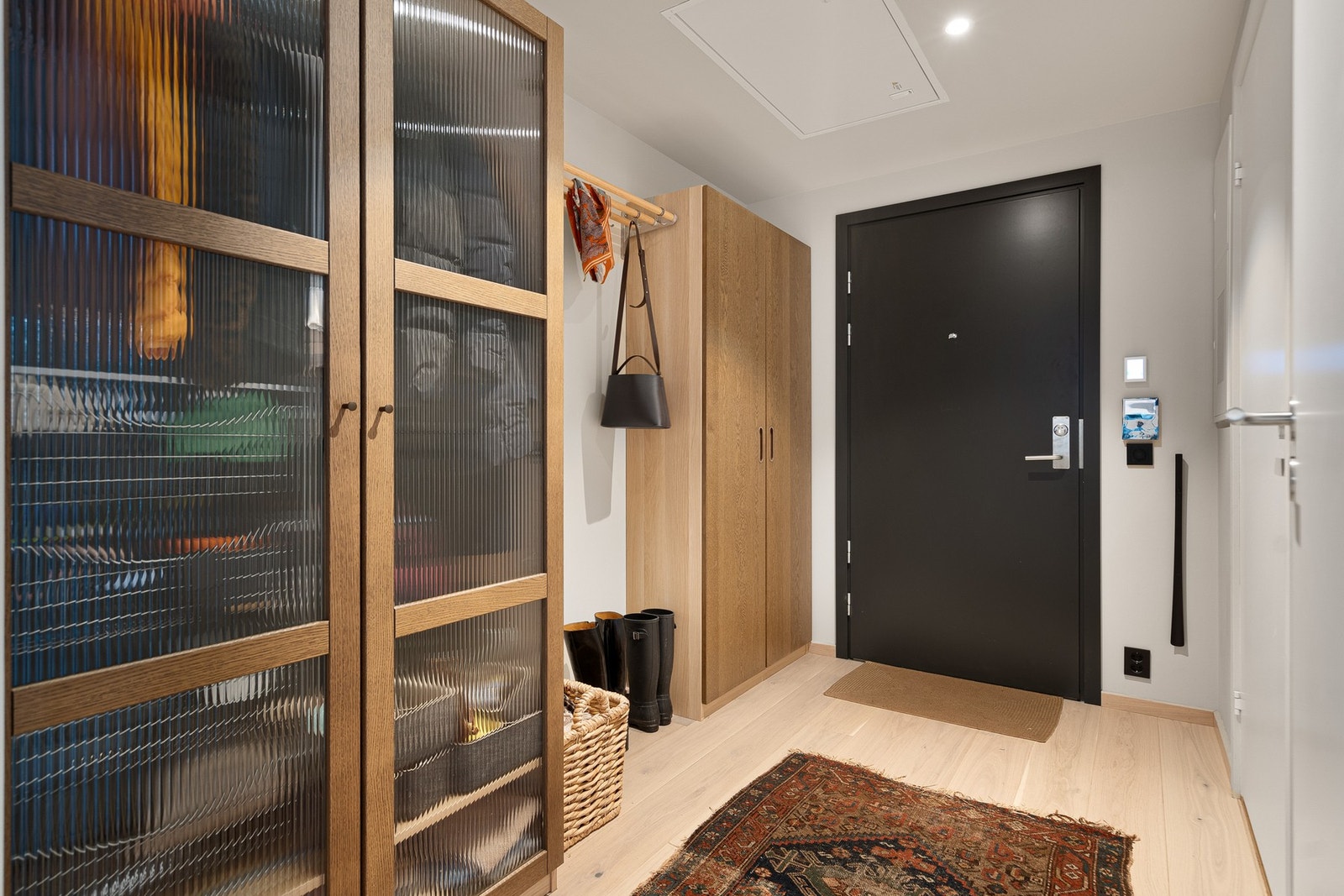 Boligen har adkomst via heis direkte fra garasje til etasjeplan. Entréen gir et meget godt førsteinntrykk og er stilrent innredet med 1-stavs parkett, hvitmalte vegger og vannbåren gulvvarme. Galleribilde