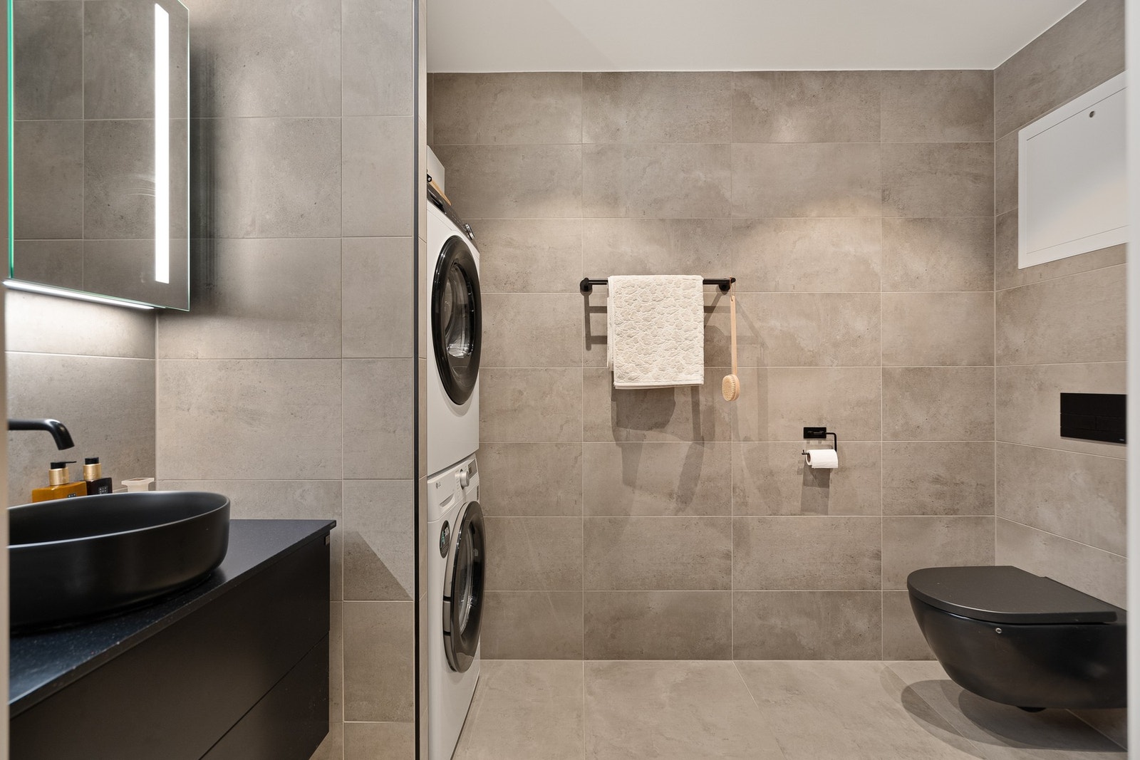 Badet er moderne og stilrent, med delikate fliser i varme, nøytrale toner som gir et tidløst uttrykk. Rommet fremstår både praktisk og gjennomført, med dusjhjørne i glass, vegghengt toalett og servant med god oppbevaringsplass i underskap. Galleribilde