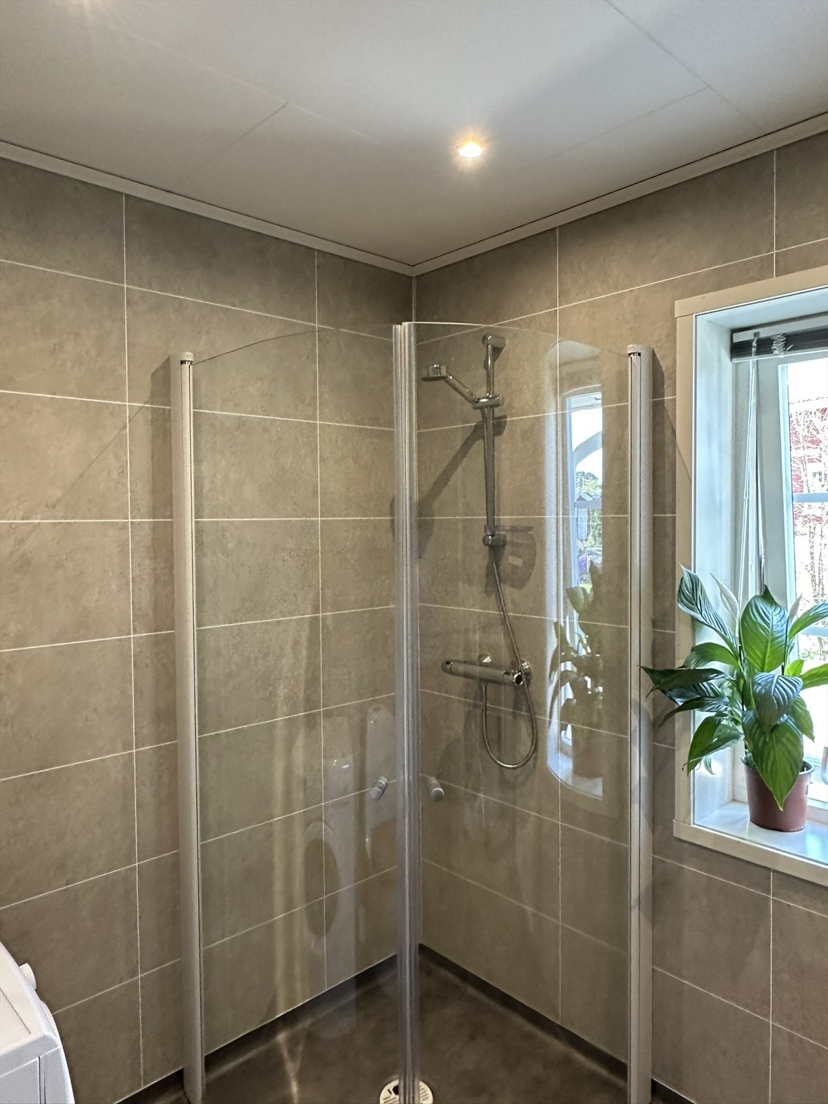 Badet er innredet med servant i baderomsinnredningen, gulvmontert toalett og et dusjhjørne med innfellbare glassdører. På badet er det opplegg for vaskemaskin og tørketrommel. Galleribilde