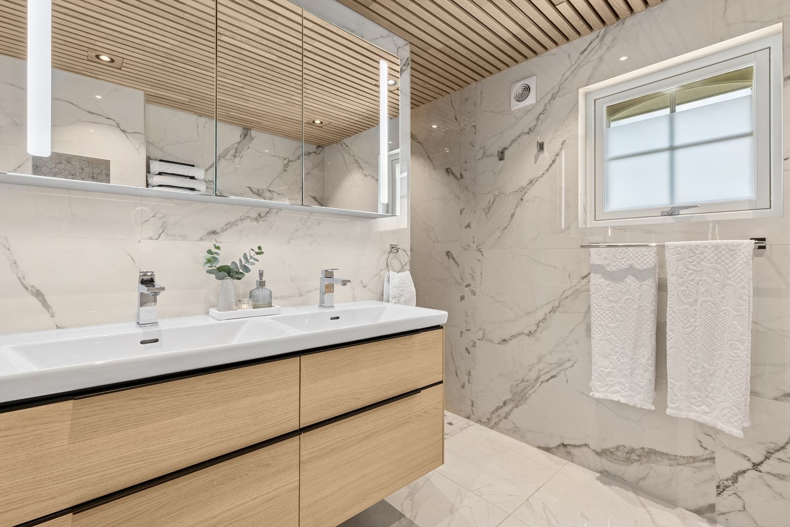 Innredningen har dobbelt servant, og over er et praktisk speil med integrert belysning. Badet kan friste med både et badekar og dusj. Galleribilde