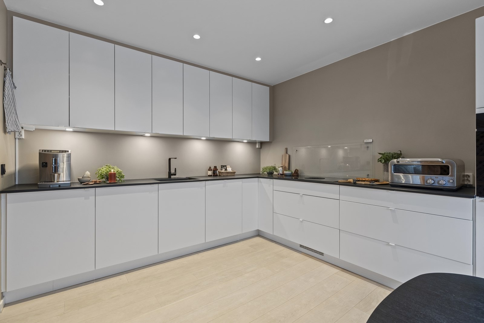 Det er godt med skap- og benkeplass. Backsplash i glass bak koketoppen. Benkeplate i kompaktlaminat i matt sort, nedfelt kum og integrert koketopp med kullfiltervifte. Galleribilde