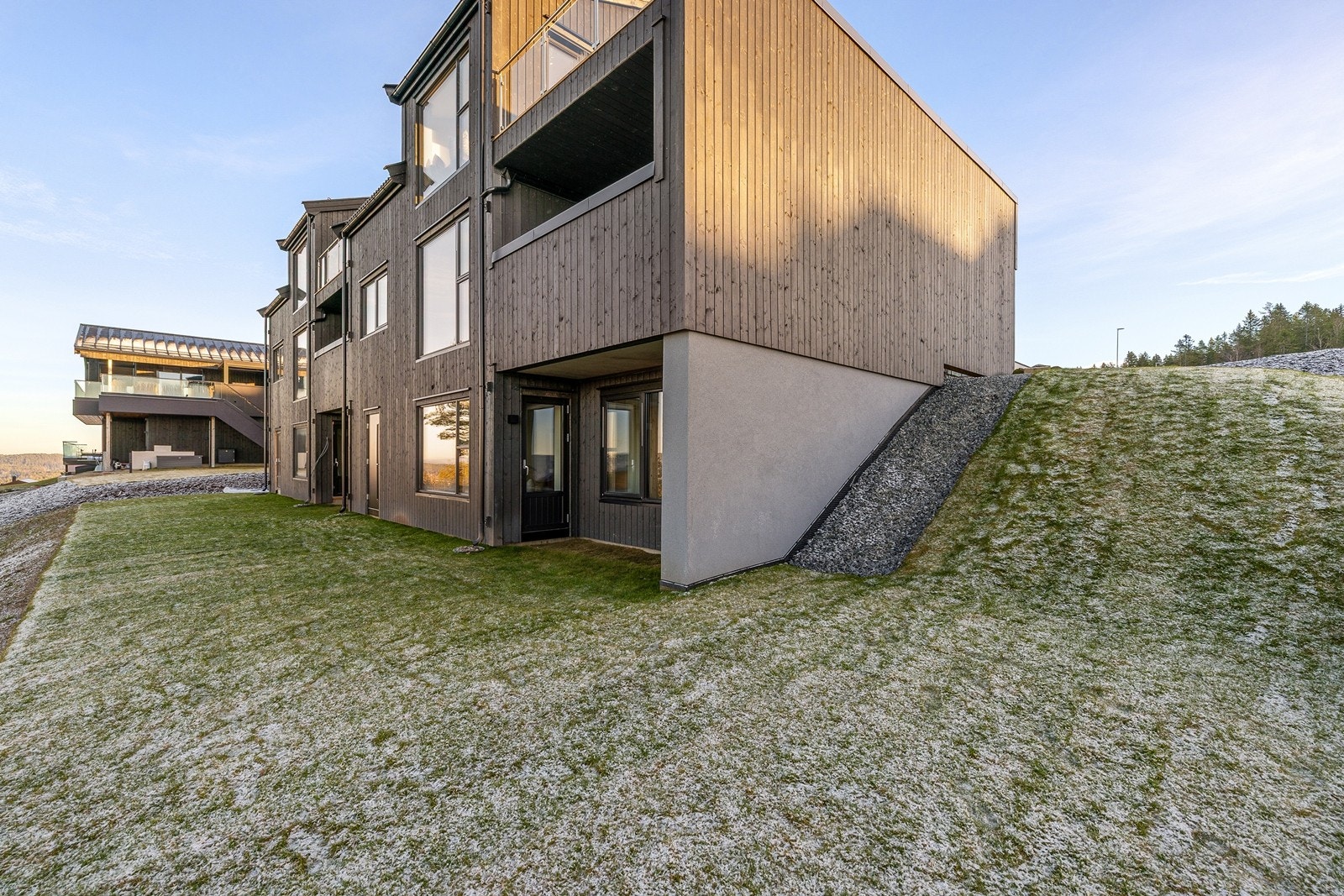 Boligen har en moderne arkitektur med mørk, stående trekledning. Galleribilde