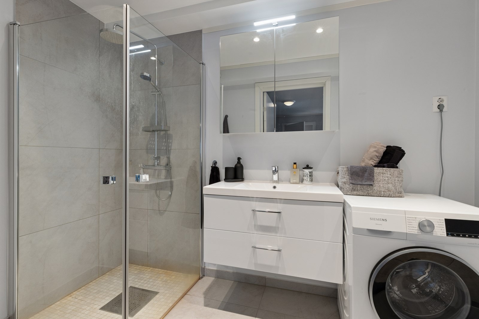 Badet i utleieleiligheten er også flislagt og har varmekabel. Servant med skuffer, speil overskap. Opplegg for vaskemaskin. Galleribilde