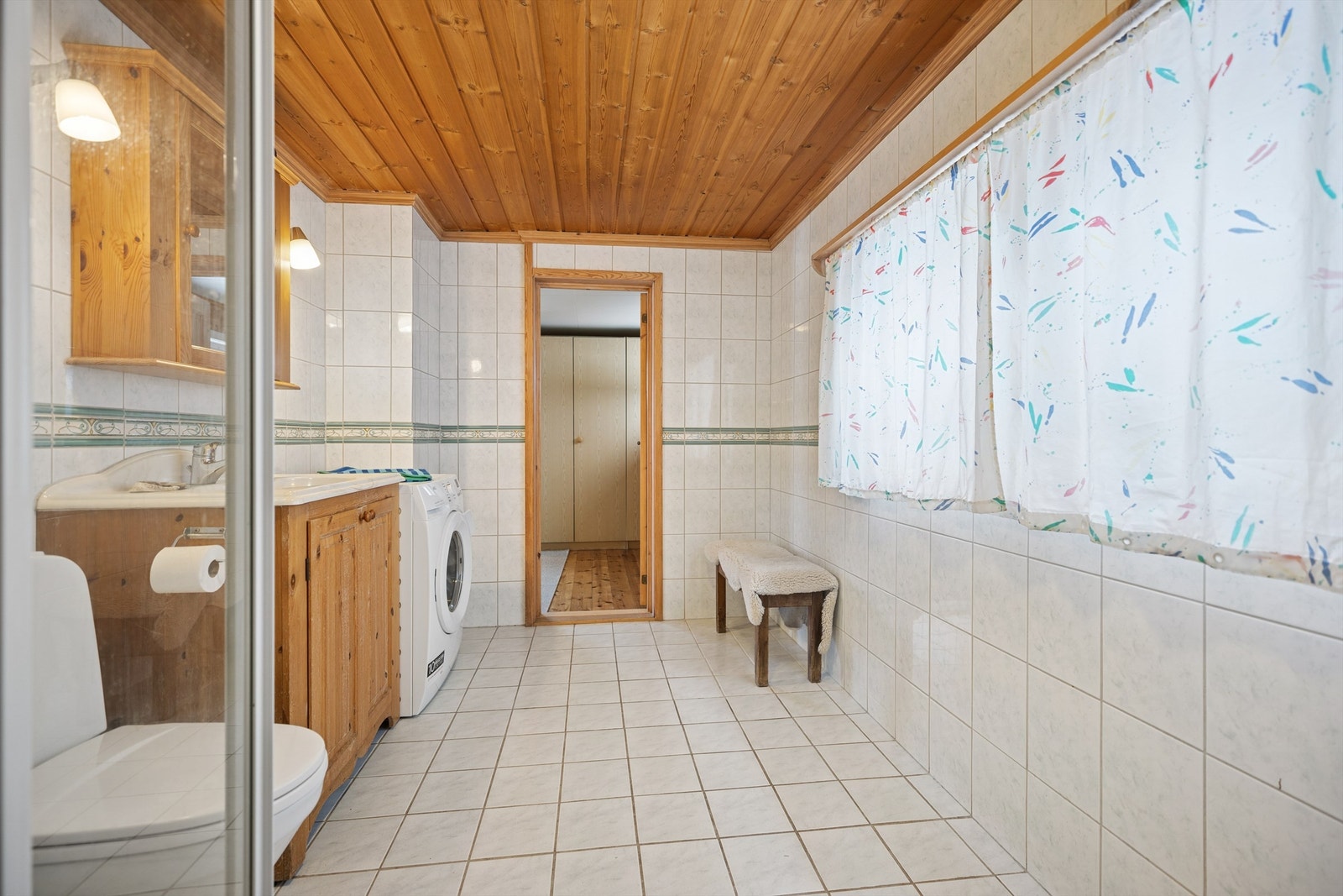 Flislagt bad med gulvvarme, dusjhjørne, servant, gulvstående toalett og opplegg for vaskemaskin Galleribilde