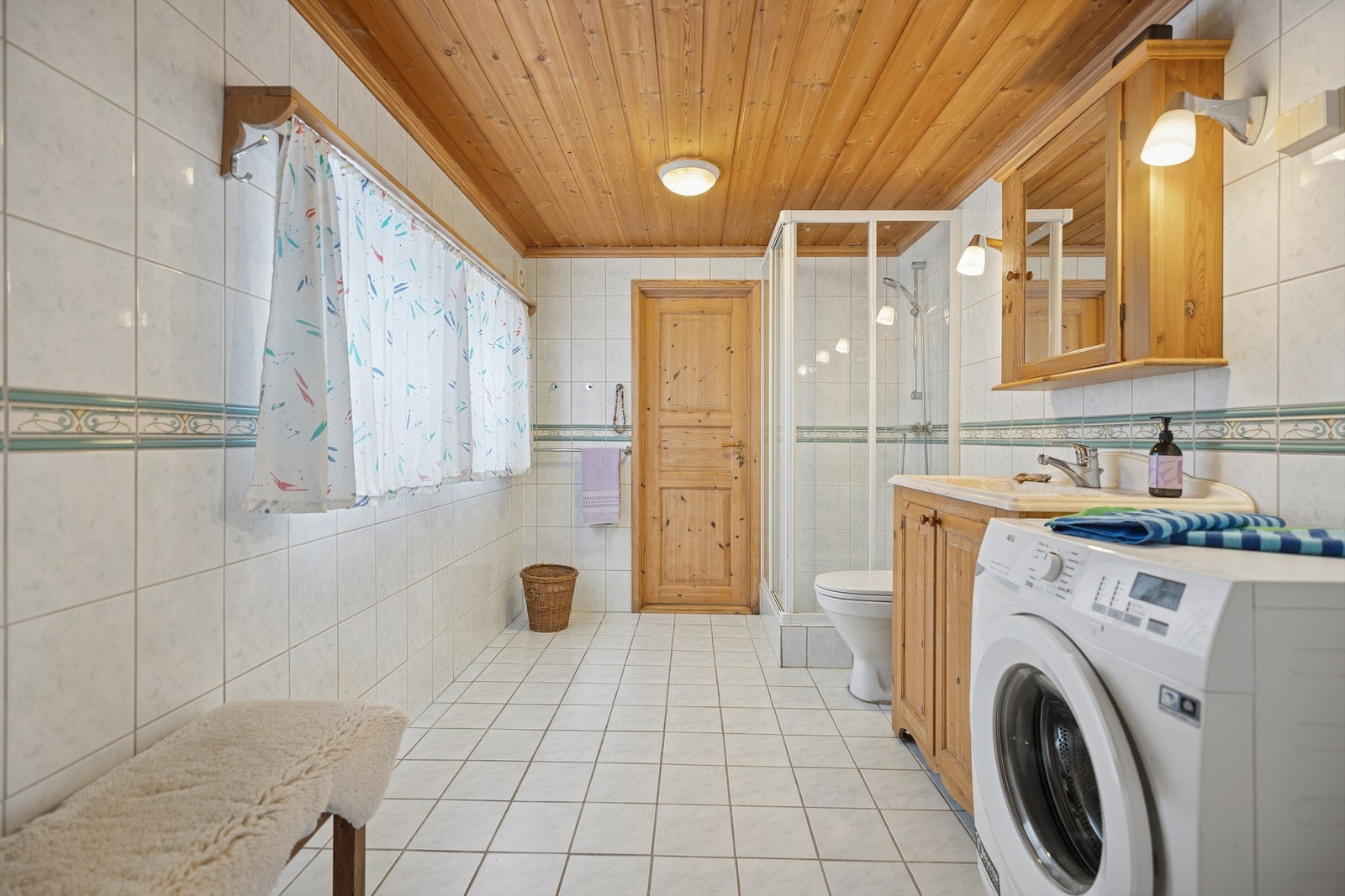 Flislagt bad med gulvvarme, dusjhjørne, servant, gulvstående toalett og opplegg for vaskemaskin Galleribilde