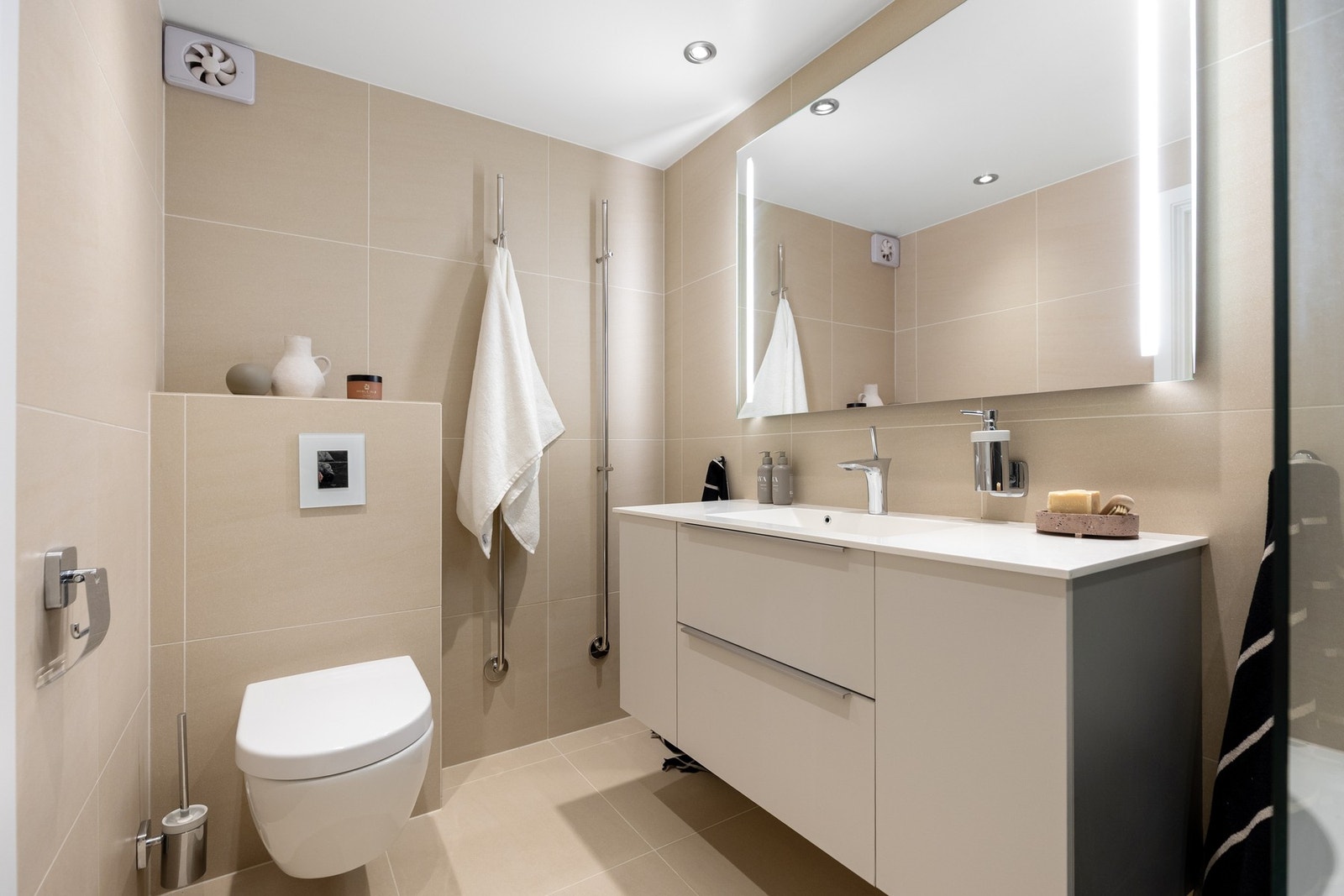 Badet er innredet med servantinnredning, vegghengt toalett og badekar med dusjløsning og glassvegg Galleribilde