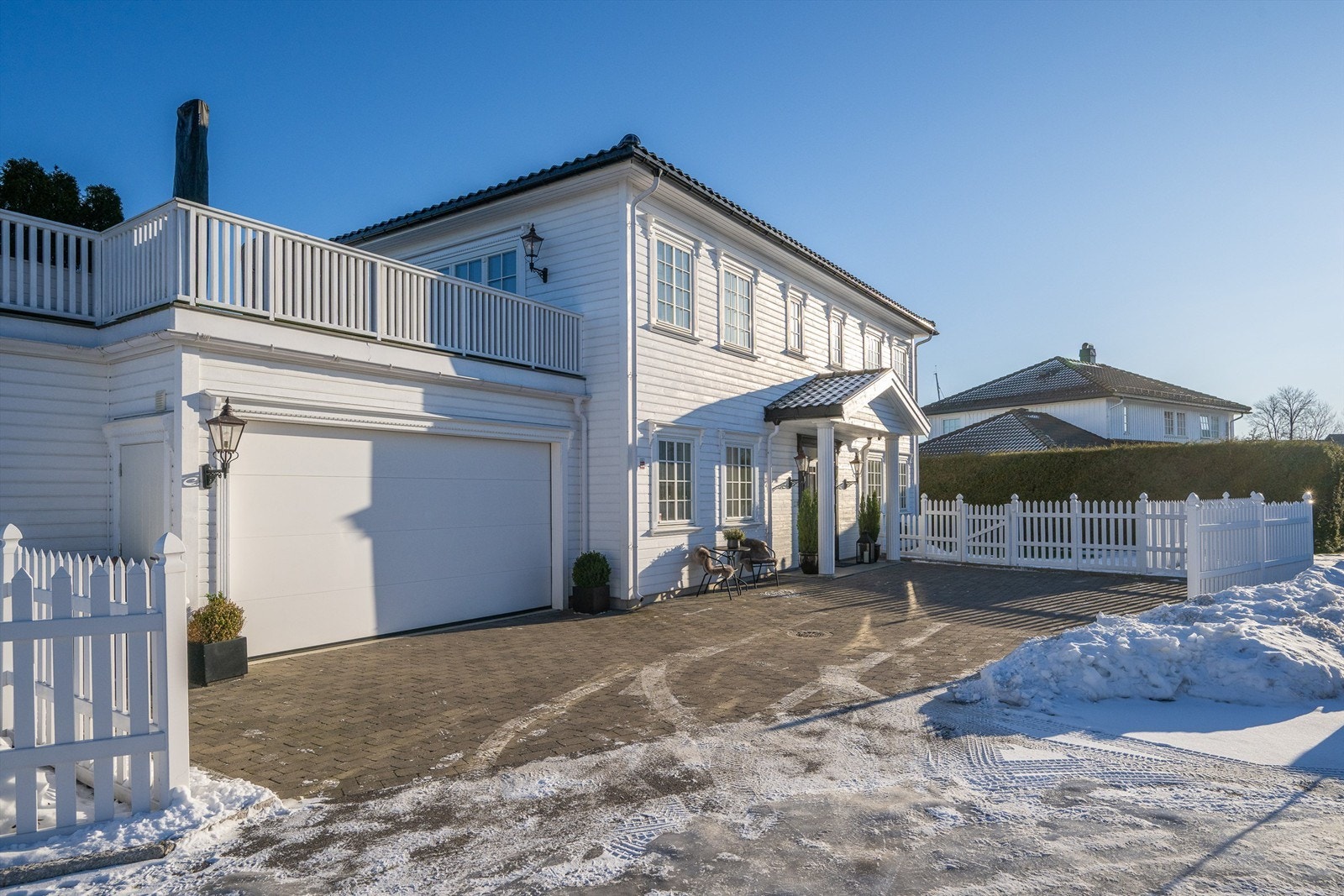 Eiendommen fremstår med et stilrent uttrykk med utebelysning, søyler, glasert takstein og pent opparbeidet hage. Galleribilde