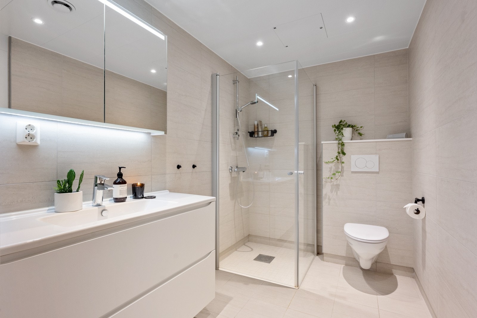 Stilrent og helfliset bad med romslig dusjsone, vegghengt toalett og servantinnredning. Galleribilde