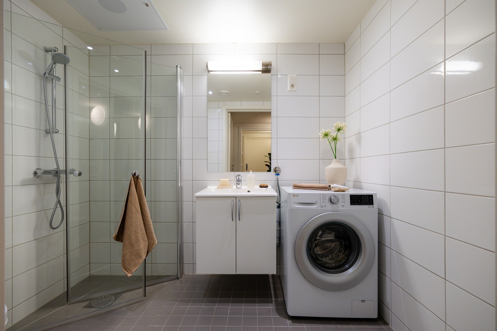 Badet er bygget opp med grå fliser med varme på gulv og lyse fliser på vegger. Vaskemaskinen medfølger. Galleribilde