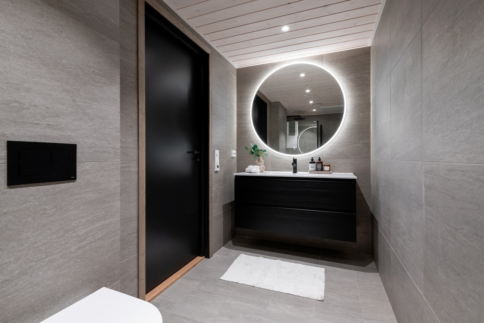 Flott flislagt hovedbad med sort innredning med ovenpåliggende servant med ett-greps armatur. Speil med rundlys og stikkontakt over servant Galleribilde