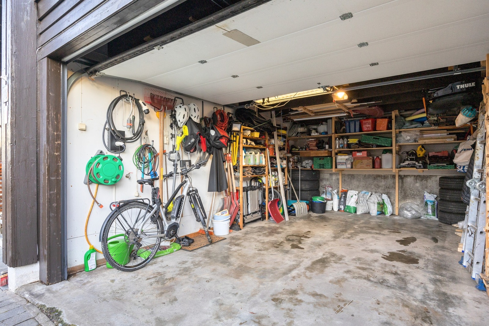 Garasjen er på ca. 21 kvm, innredet med hyller elbillader og motorisert leddport. Galleribilde