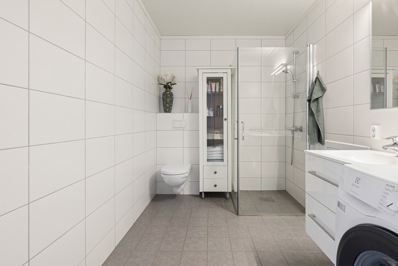 Rommet er innredet med en nedfelt servant, vegghengt toalett og et dusjhjørne med innfellbare dusjvegger. Galleribilde