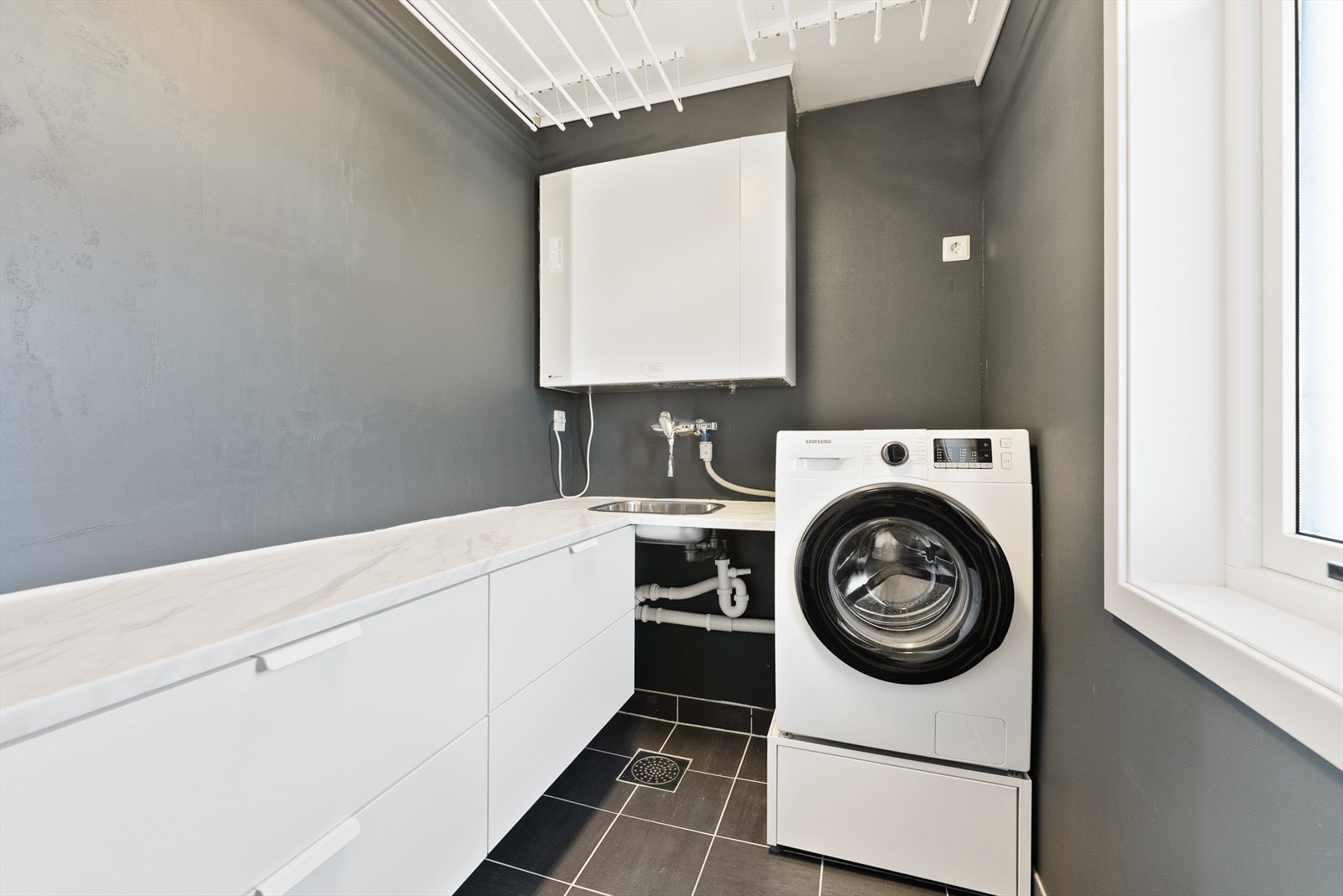 Lyst og funksjonelt vaskerom med moderne innredning. Praktisk benkeplass, vaskemaskin, og oppbevaringsmuligheter. Ideelt for en effektiv hverdag. Galleribilde