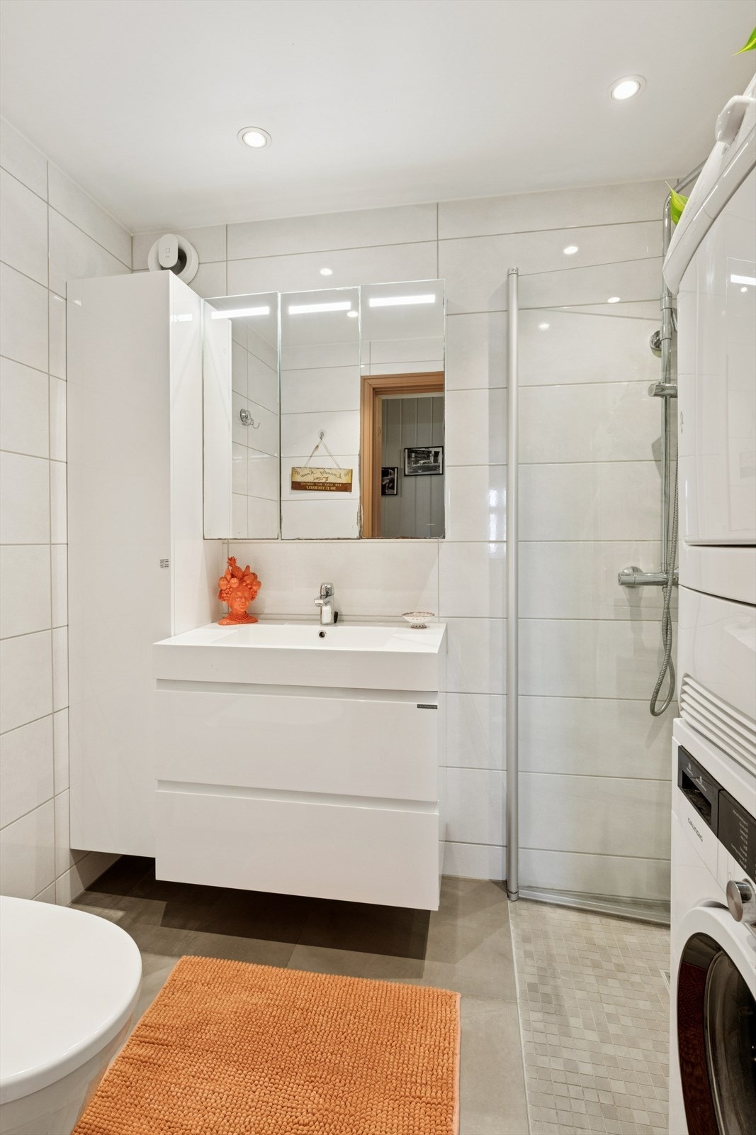 Badet er innredet med toalett, dusjhjørne med glassvegger, veggskap, samt baderomsinnredning med servant og speilskap. Galleribilde