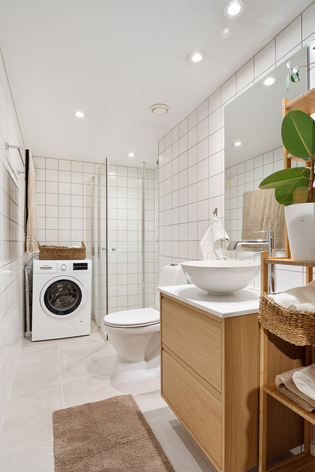 Badet er innredet med servantskap med glatte, folierte fronter og heldekkende servant, speil på vegg, gulvmontert toalett samt dusjhjørne med svingdører og termostatstyrt blandebatteri. Galleribilde