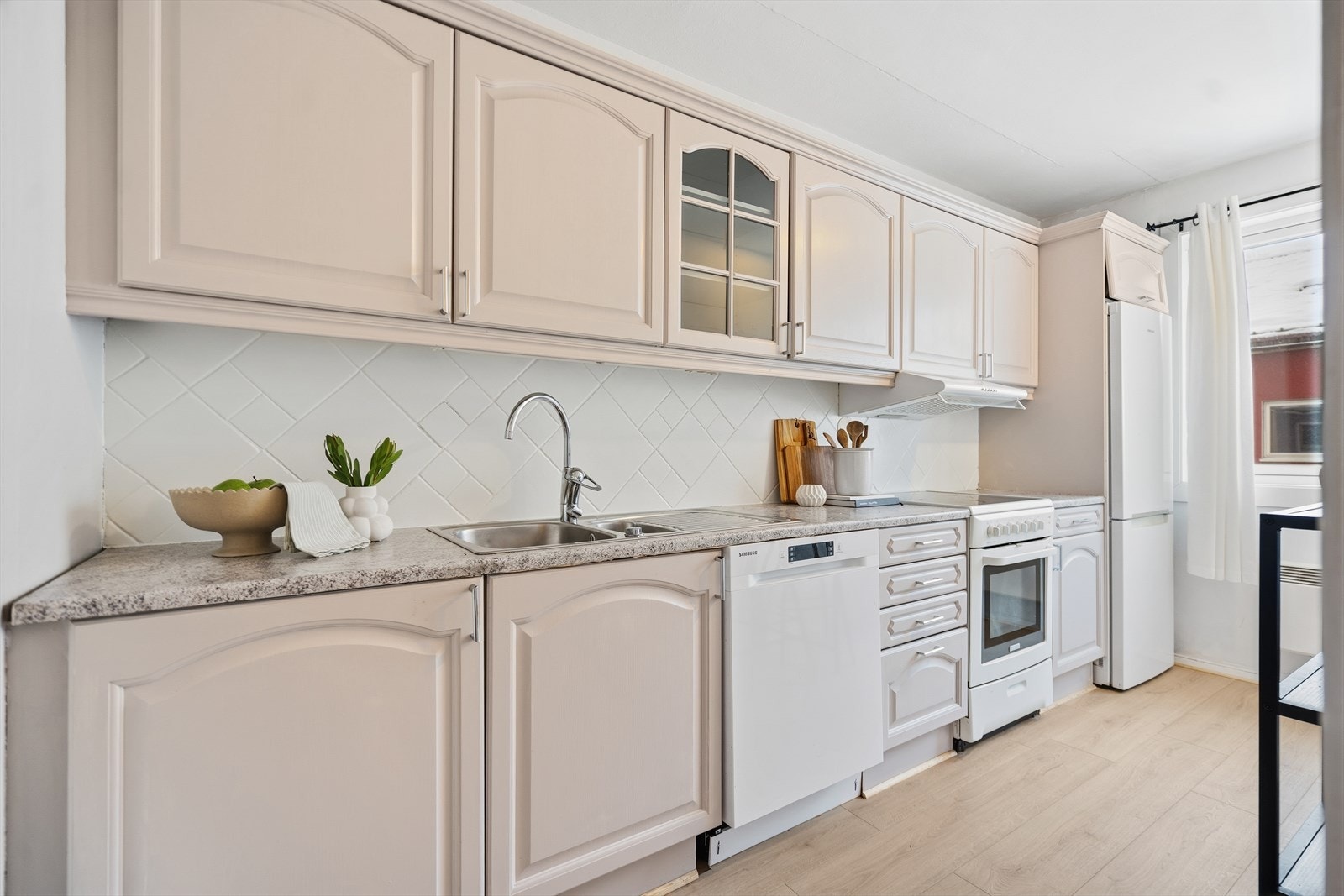 Kjøkkenet har lyse profilerte flater og benkeplate av laminat. Kjøkkenet er utstyrt med kjøl/fryseskap, oppvaskmaskin, komfyr og kjøkkenventilator med avtrekk ut av leilighet. Galleribilde