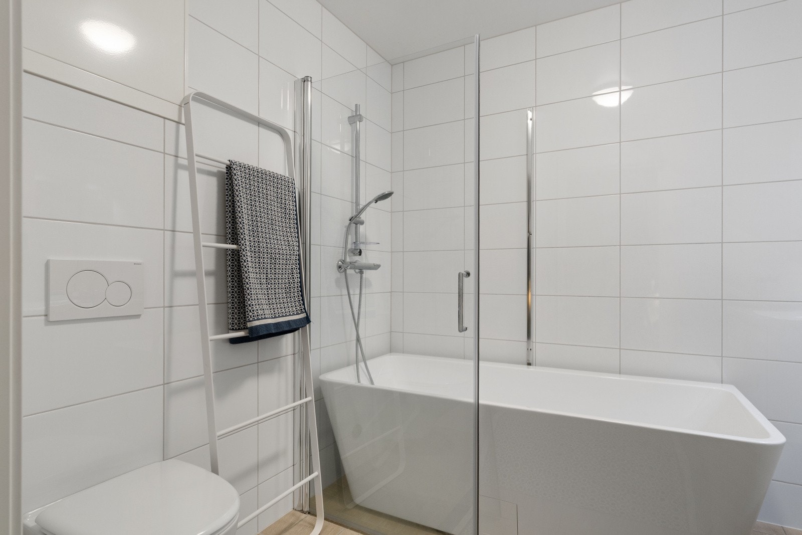 Pent flislagt baderom utstyrt med vegghengt toalett, baderomsinnredning og badekar. Galleribilde