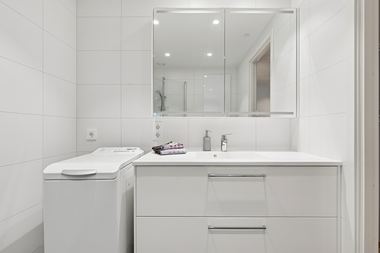 Baderomsinnredning med skuffer, heldekkende servant og overskap med speilfronter. Opplegg for vaskemaskin og tørketrommel. Galleribilde