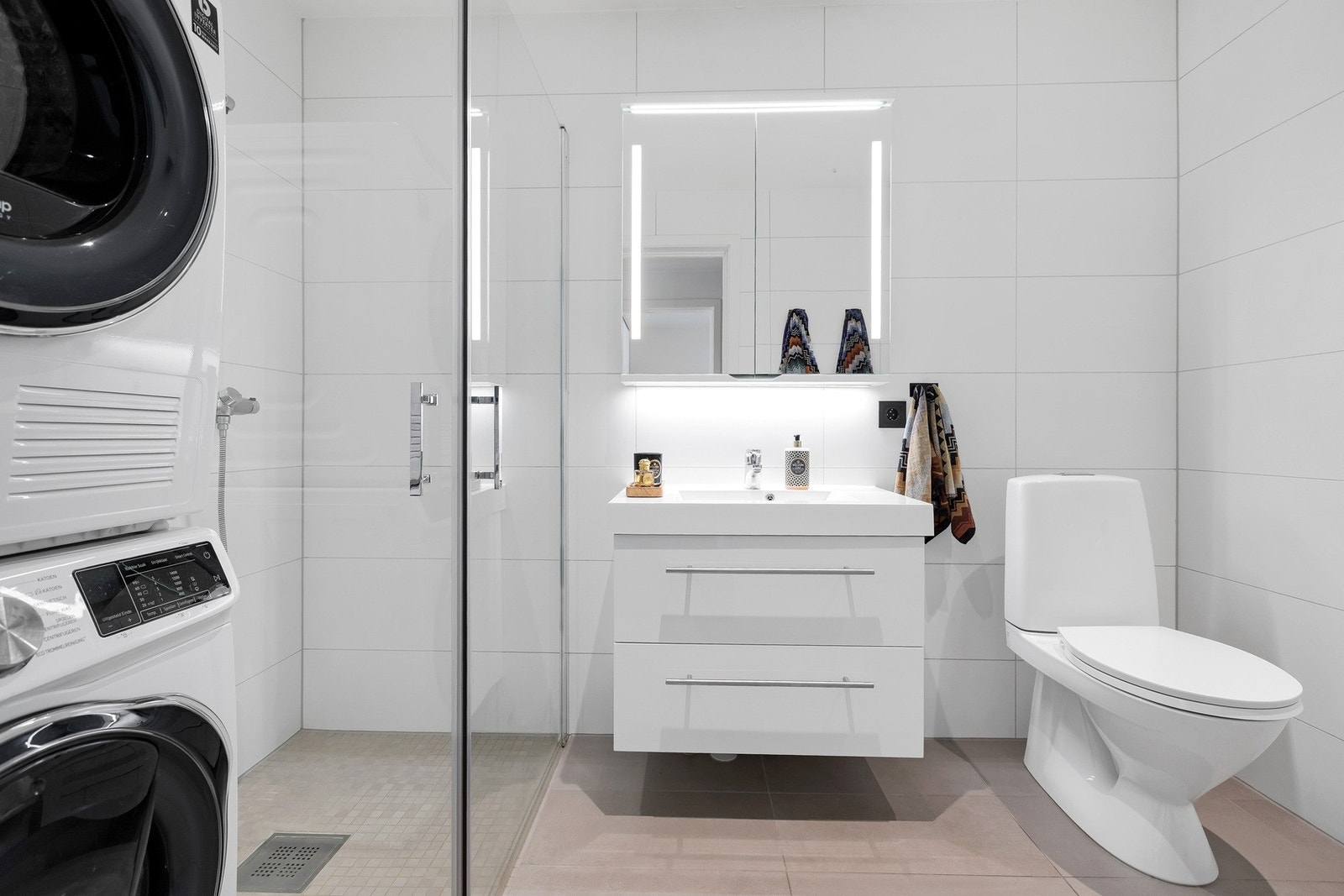 Praktisk og delikat baderom med dusjhjørne, vegghengt innredning og plass til både vaskemaskin og tørketrommel. Galleribilde