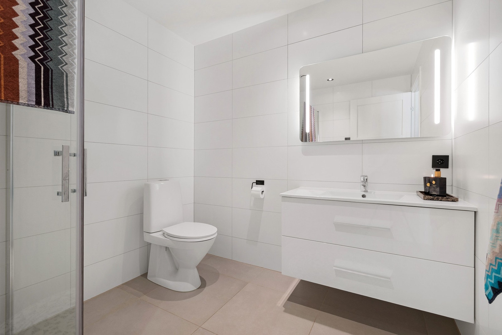 Lyst og moderne bad med elegante fliser, servant med innredning og speil med integrert belysning. Galleribilde