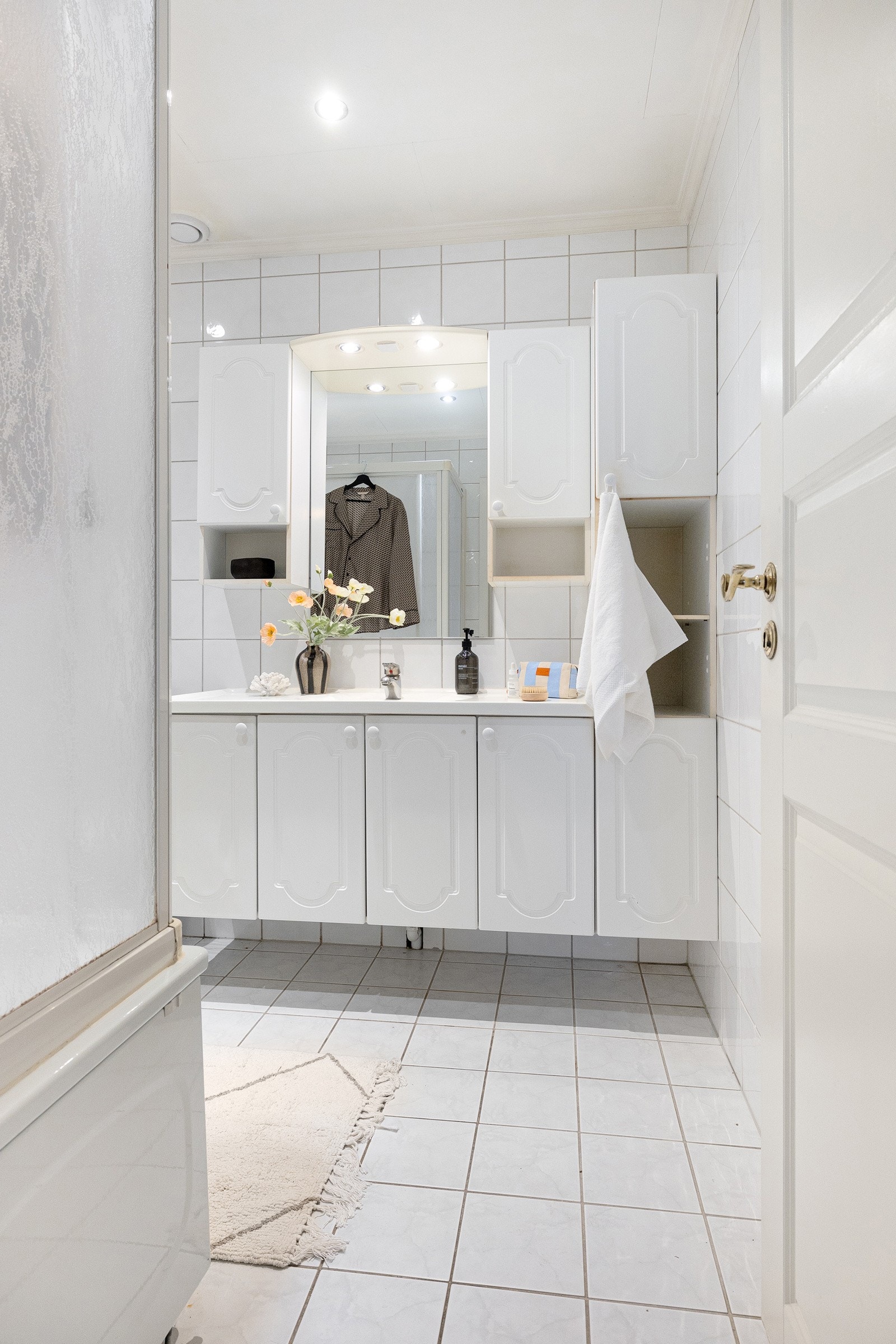 Eldre bad innredet med servant med underskap, høyskap samt speil med integrert belysning og sideskap. Galleribilde